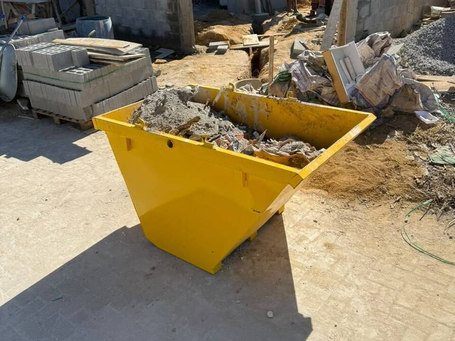 Mini caçamba amarela cheia de entulho em obra pequena